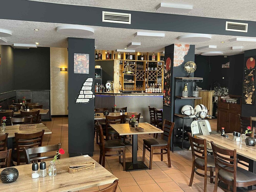 Dunkler Gastraum mit Weinregal und eingedeckten Tischen