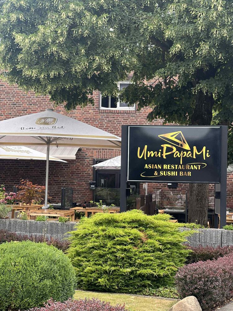 Außenschild „UmiPapaMi – Asian Restaurant & Sushi Bar“ hinter einer Hecke